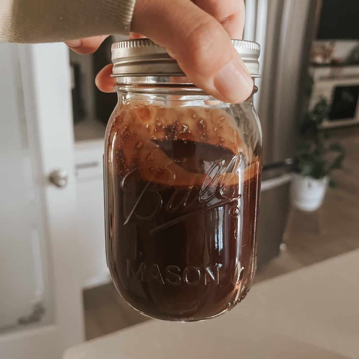 holding up a jar of homemade chocolate syrup in a mason jar