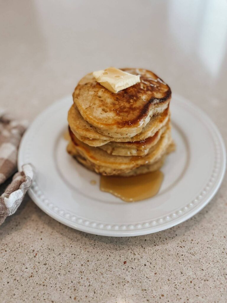 fluffy sourdough pancakes stacked on top of each other with butter and maple syrup on a white plate 