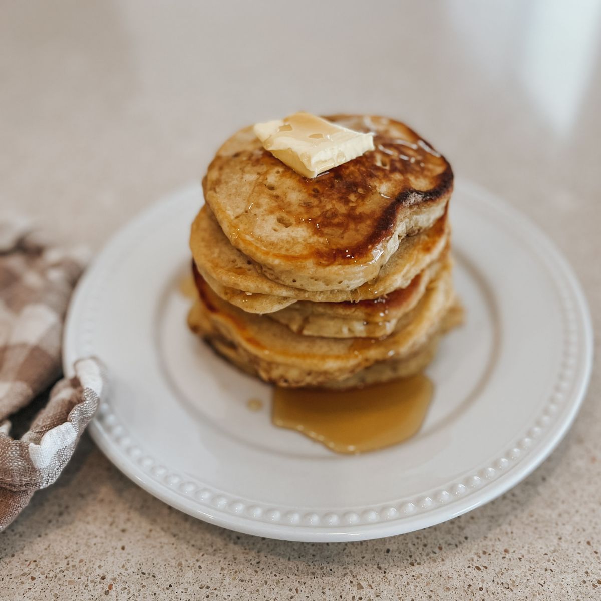 fluffy sourdough pancakes staked on top of each other on a white plate with butter and maple syrup