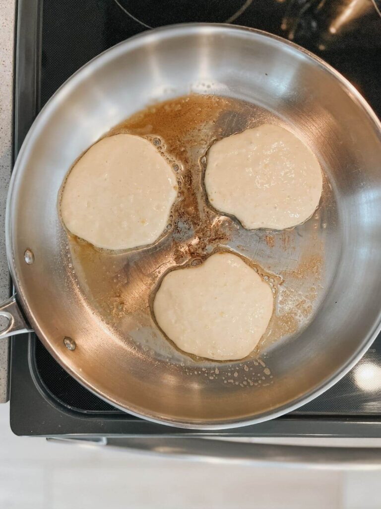 3 fluffy sourdough pancakes in a stainless steel pan getting ready to cook