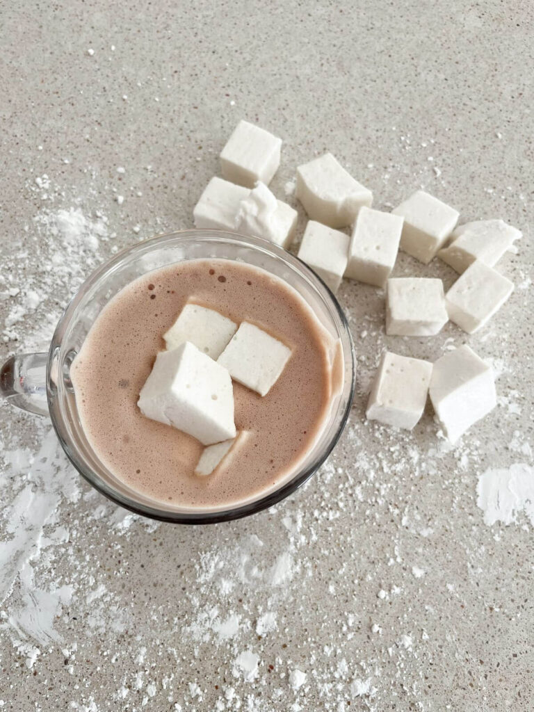 marshmallows cut up and by the side of a cup of hot chocolate with marshmallows on top