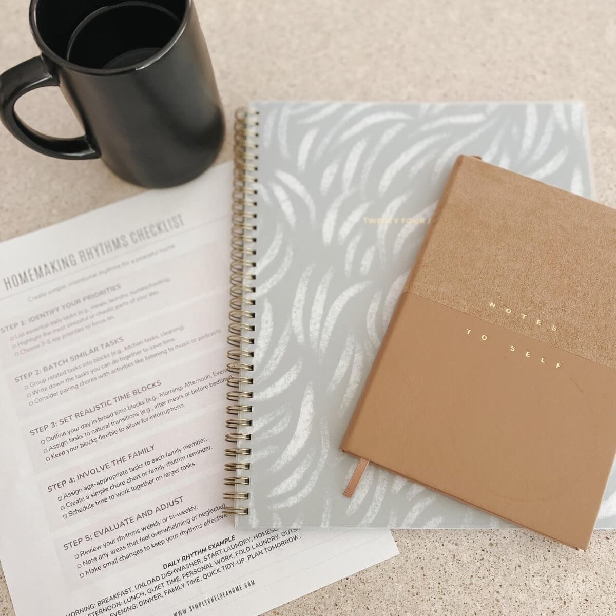 planner, notebook, homemaking rhythms checklist on counter with a black coffee mug