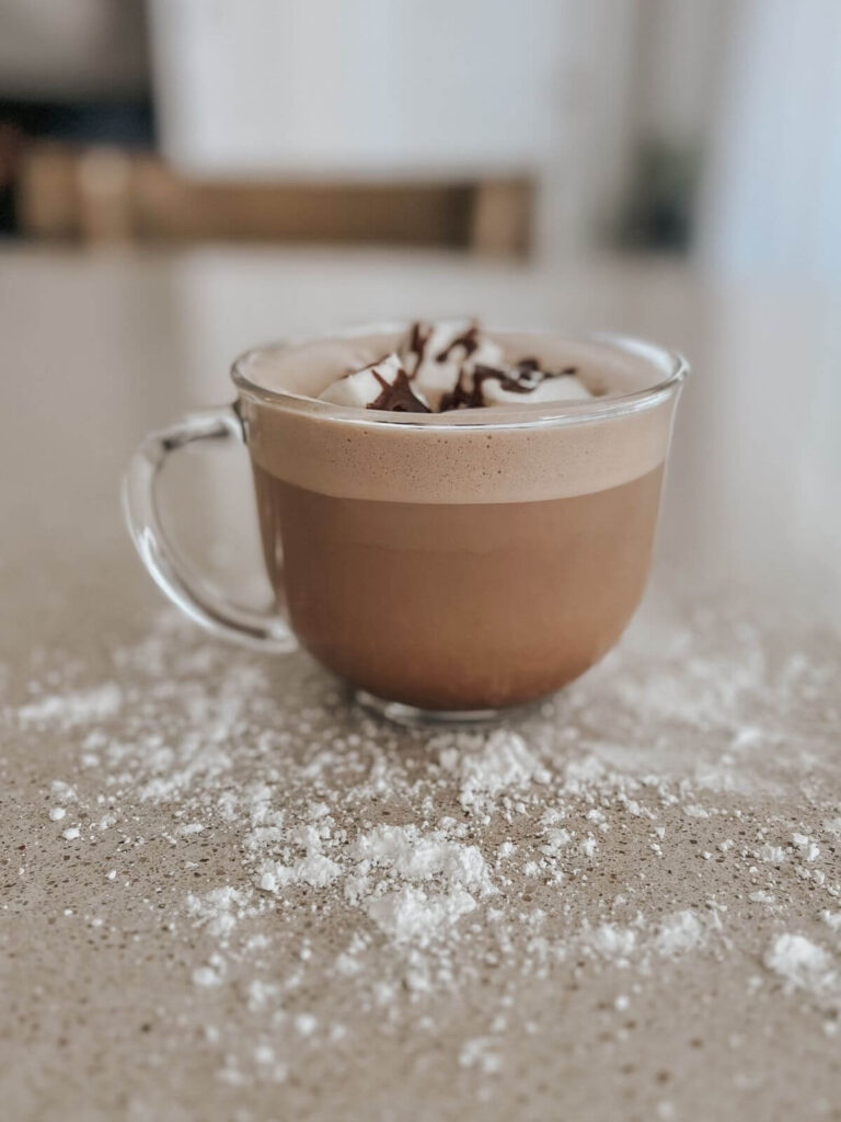 hot chocolate in a glass mug with homemade marshmallows on top with chocolate drizzle