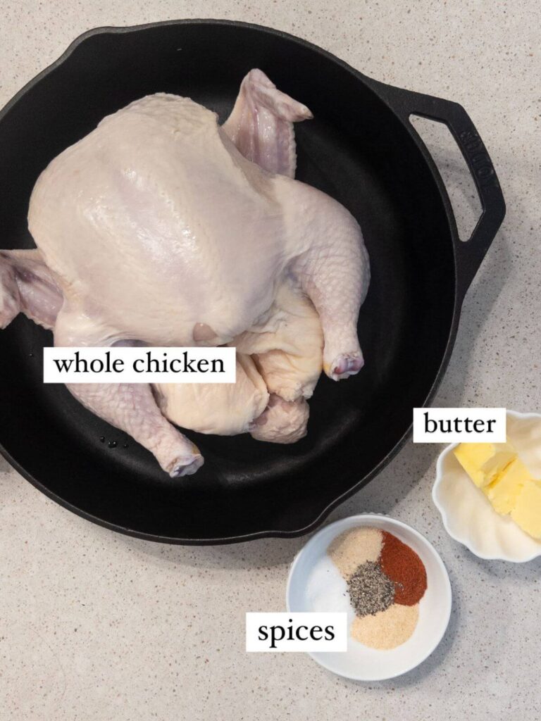 flat-lay of the ingredients needed for the recipe: whole chicken in a cast iron pan, butter, herbs and spices