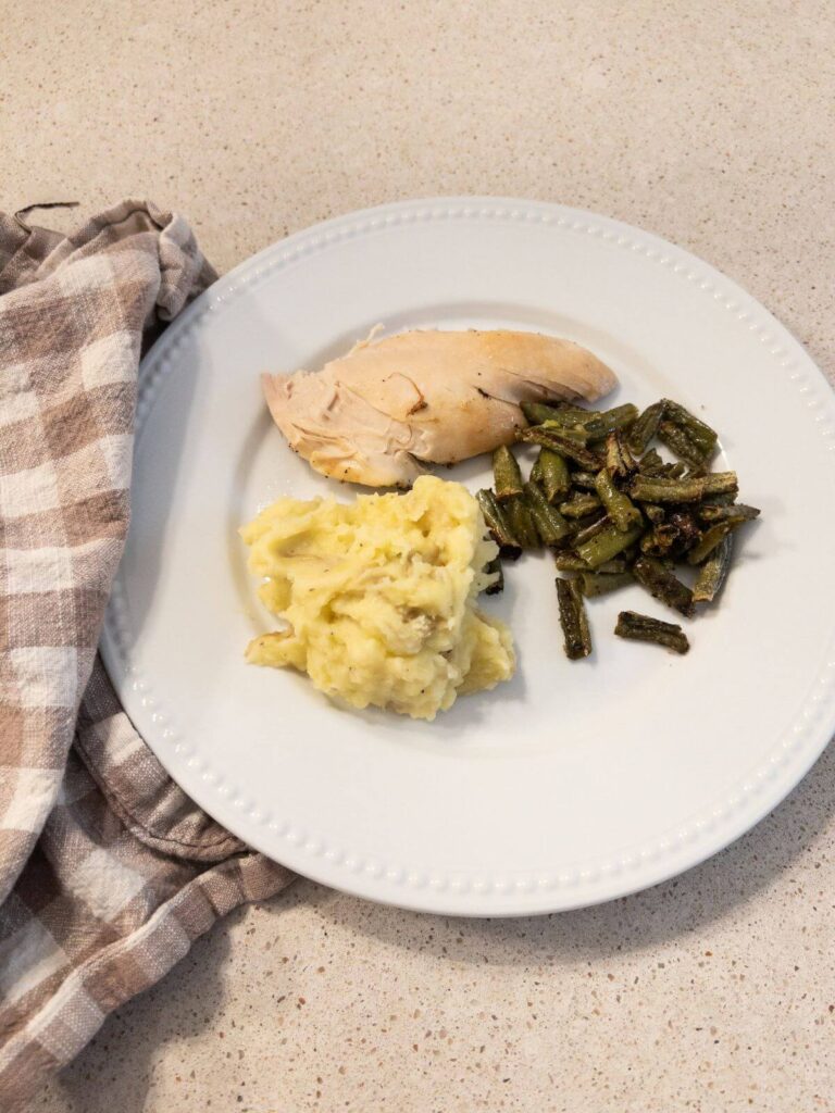 chicken on a white plate with green beans and mashed potatoes with a checkered napkin. 
