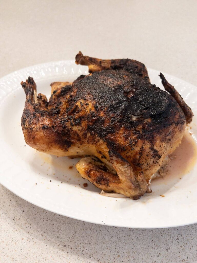 whole chicken resting on a white platter after fully being cooked. 