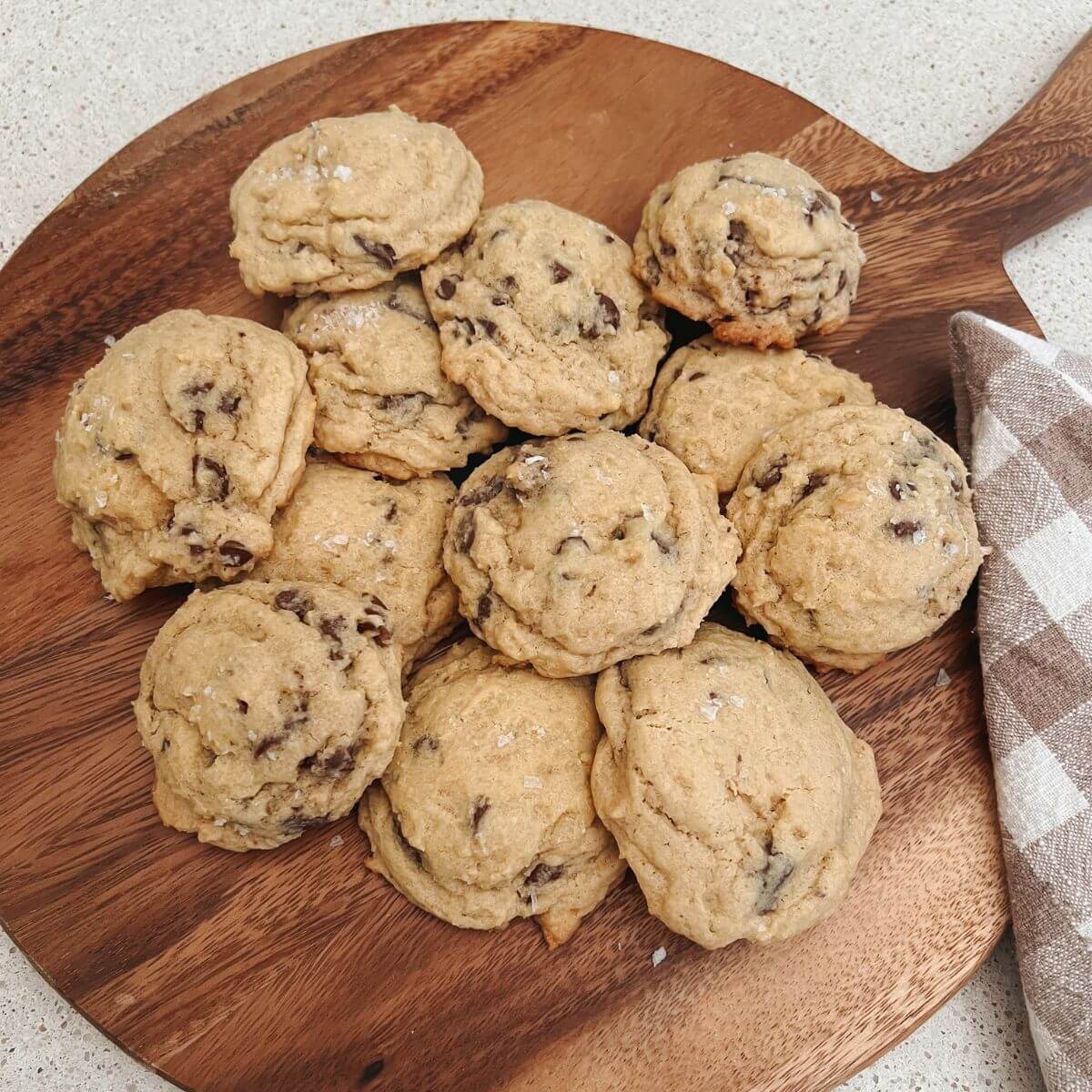 The Best Sourdough Chocolate Chip Cookies on a wooden cutting board with a plaid towel