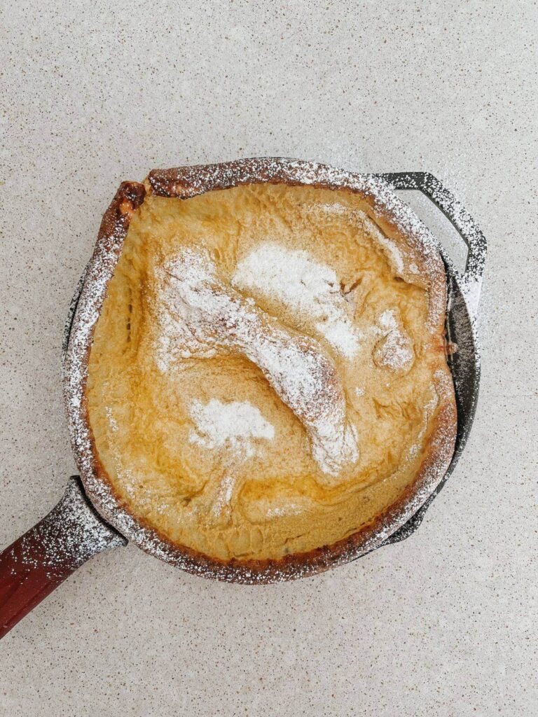 dutch baby pancake in a cast-iron pan baked and topped with powdered sugar