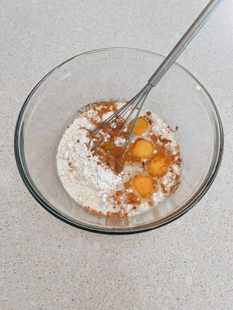 blending all the ingredients in a glass bowl: eggs, flour, salt, vanilla, cinnamon, milk with a stainless steel whisk