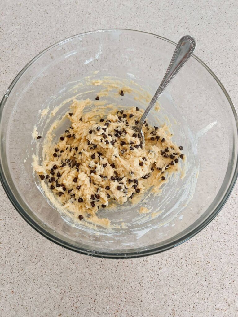 The muffin batter full together in a glass bowl with a silver spoon. 