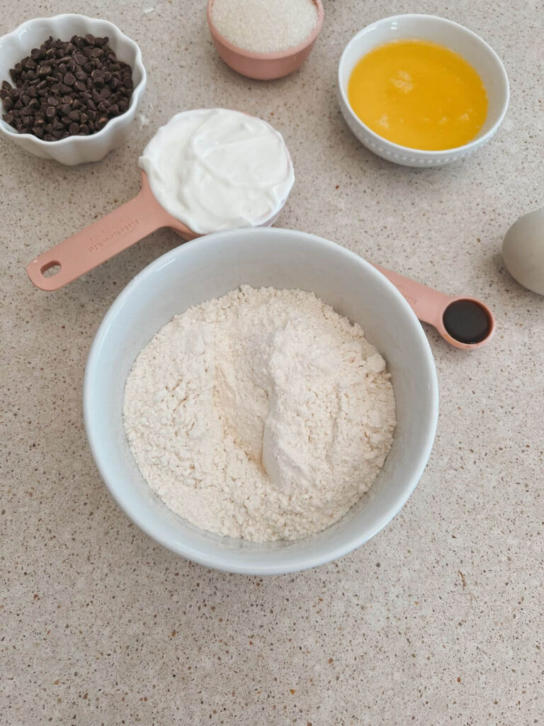 Dry ingredients for the muffins in a white bowl with the wet ingredients in the background