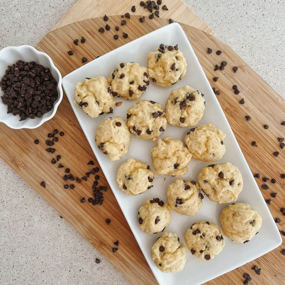 mini chocolate chip muffins on a white rectangular serving platter on a cutting board with mini chocolate chips sprinkled around and a small white bowl of mini chocolate chips