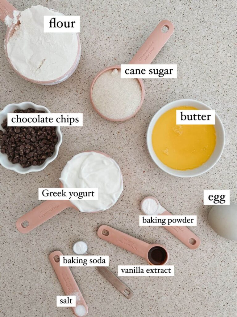 flat-lay of the ingredients needed to make the recipe: flour, greek yogurt, can sugar, butter, egg, baking powder, vanilla extract, baking soda, salt, chocolate chips
