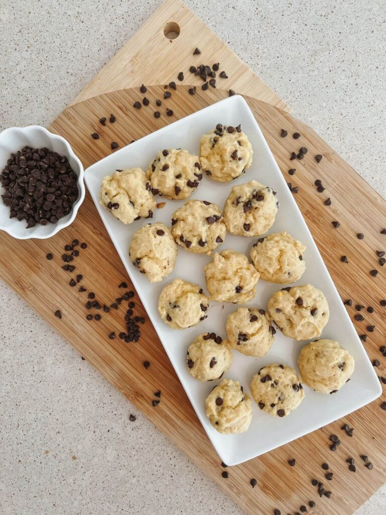 mini chocolate chip muffins on a white rectangular serving platter on a cutting board with mini chocolate chips sprinkled around and a small white bowl of mini chocolate chips
