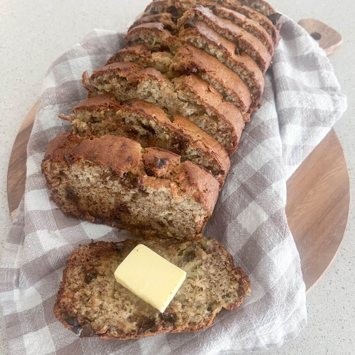 best banana bread sliced with butter on a plaid towel on a cutting board