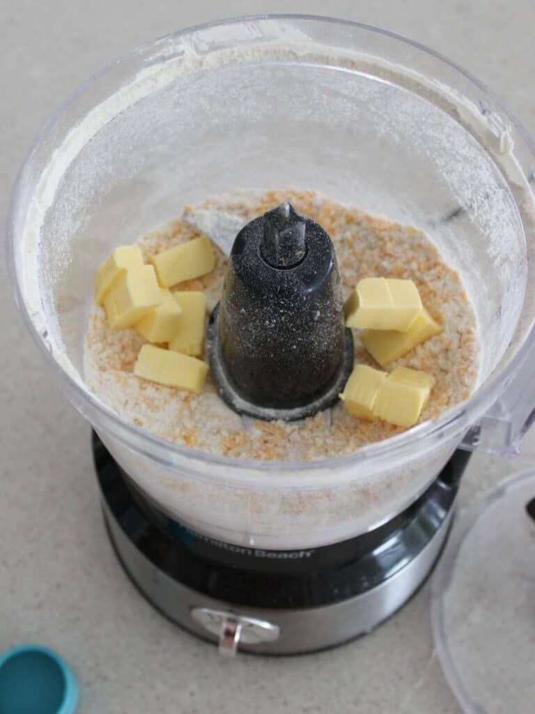 Adding butter to the cheese mixture in the food processor. 