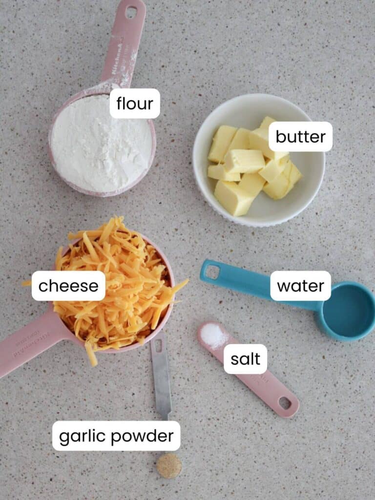 An ingredient flat-lay of what is needed to make the cheese crackers: flour, butter, water, salt, garlic powered, cheese