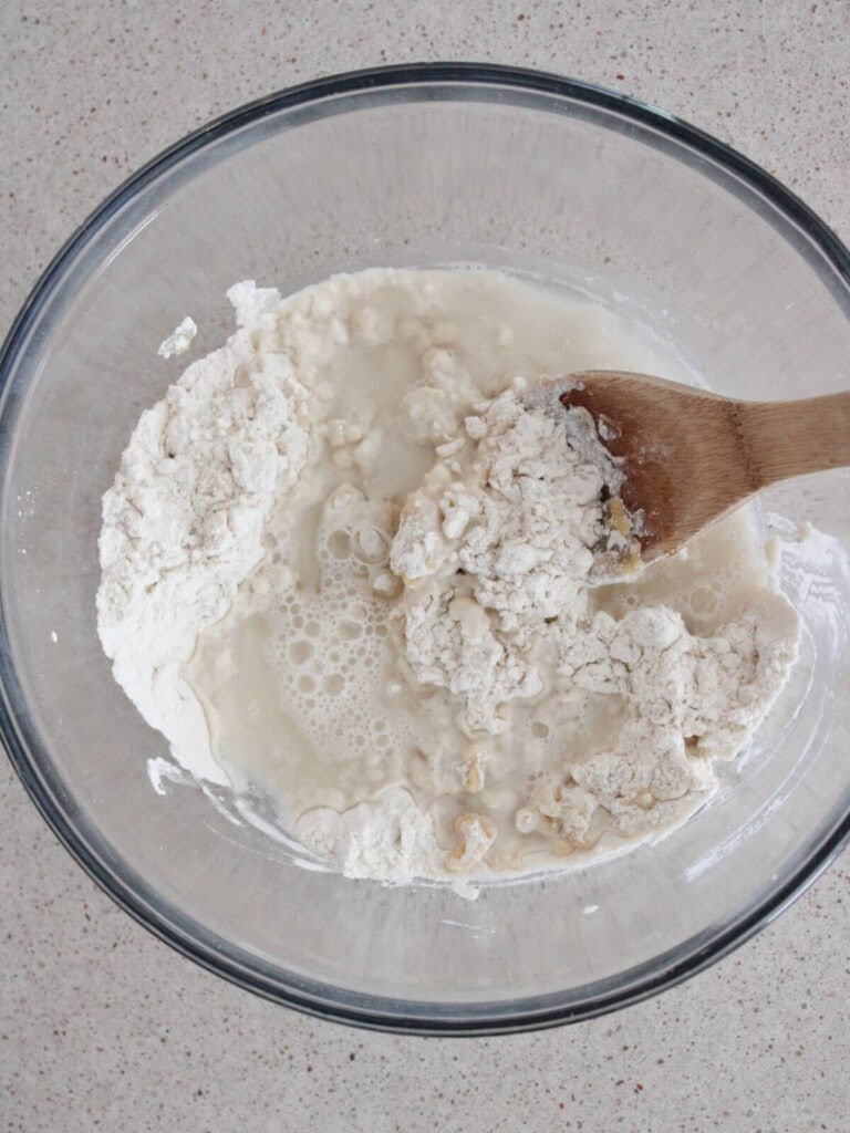 Water added to the dough mixture with a wooden spoon in a glass bowl. 