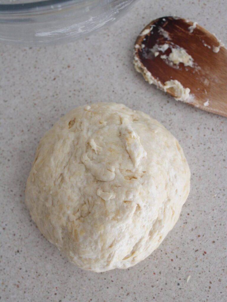 Dough resting in a ball on the counter with a wooden spoon next to it. 