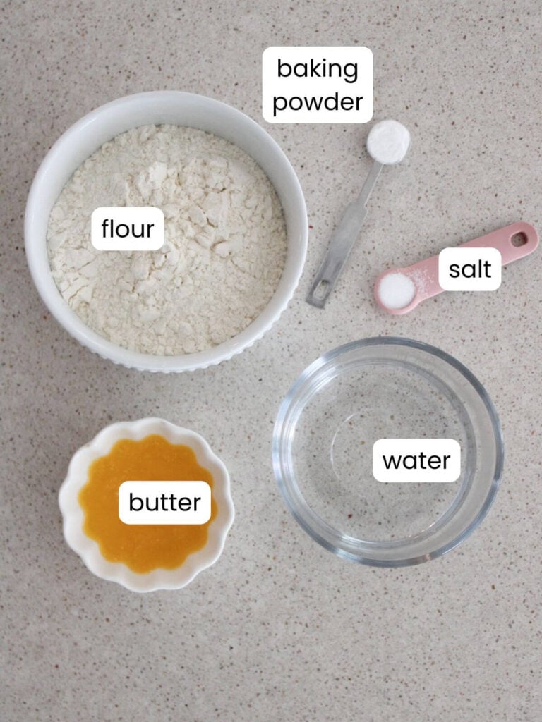 A flat-lay of the ingredients needed for the recipe: flour, baking powder, salt, water, butter. 