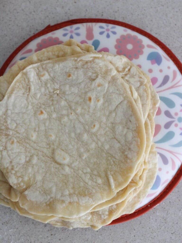 Tortillas all cooked and ready to eat on top of a tortilla warmer. 