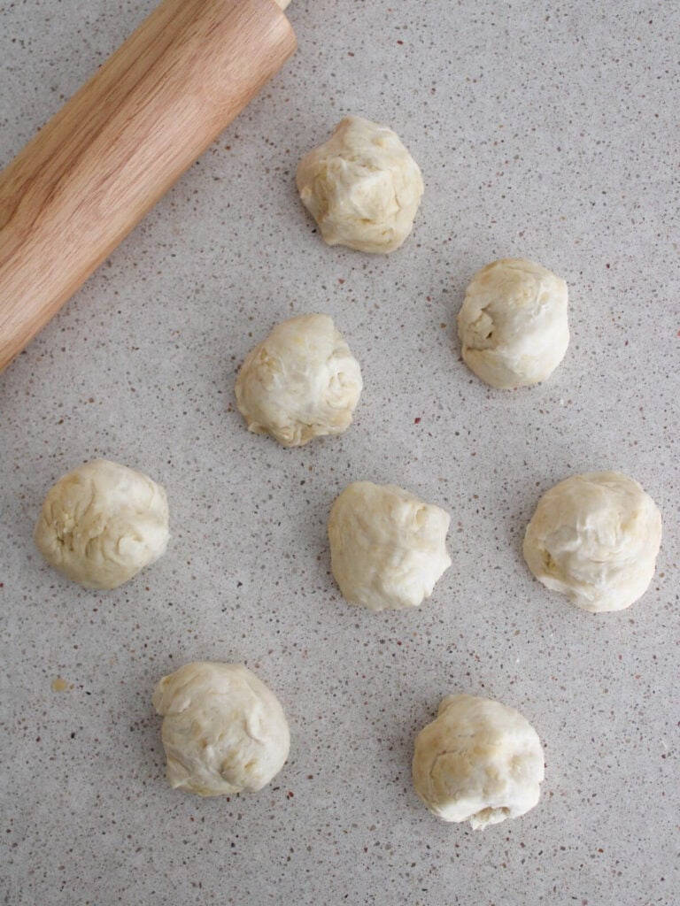 Dough divided into 8 small balls ready to roll out with a rolling pin next to it. 
