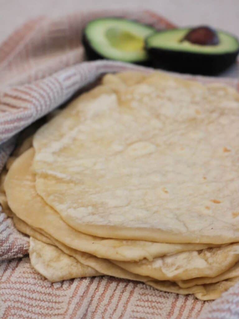 Easy Homemade Tortillas stacked inside a pink towel with an avocado behind them.