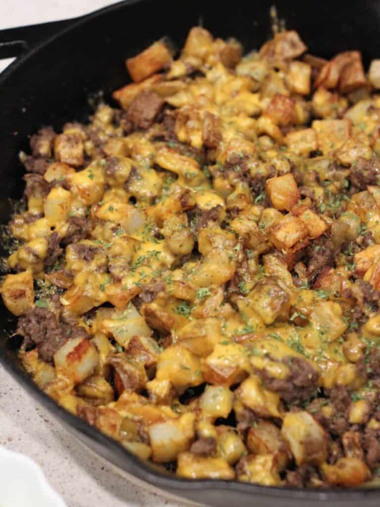 Side view and close up of the cheesy potato bowl with ground beef in a cast-iron skillet with parsley on top 