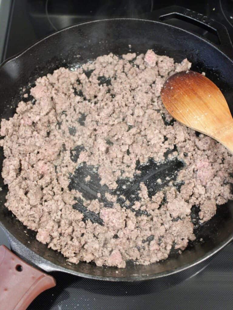 Ground beef being cooked in a cast iron pan and seasoned. 