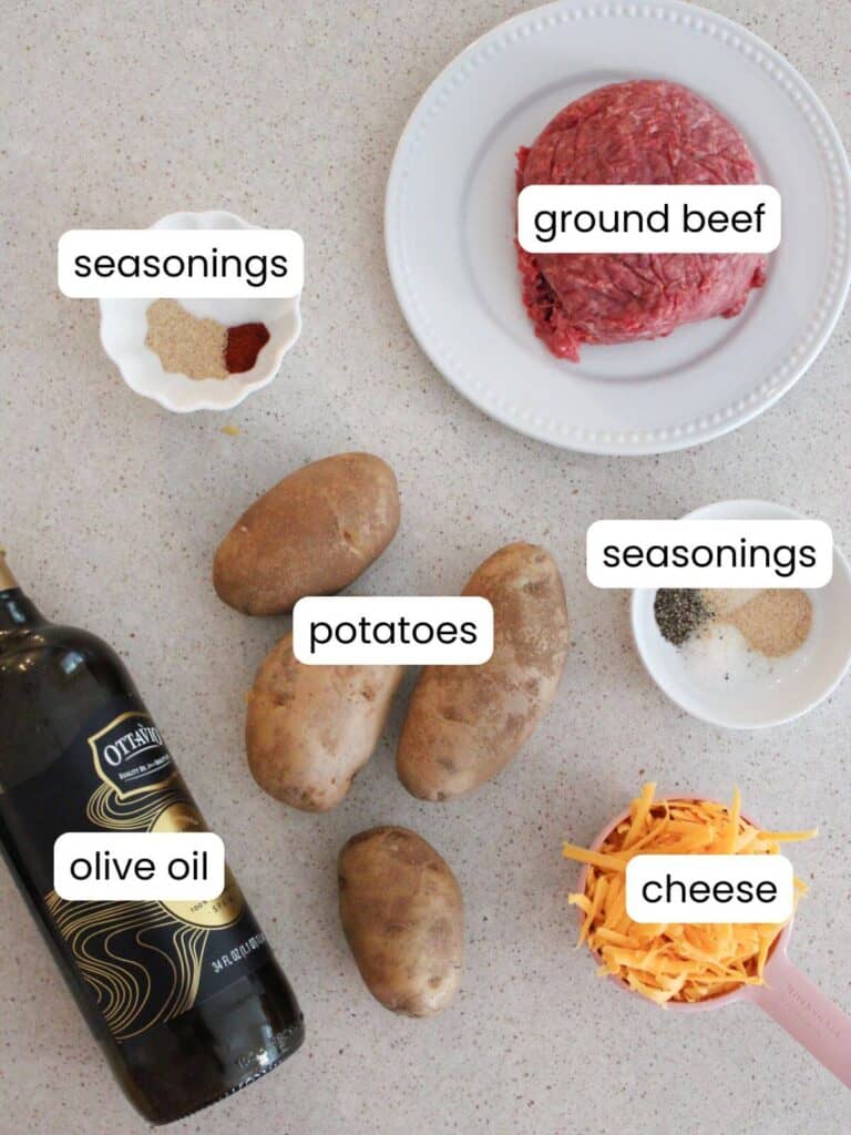 A flatlay of the ingredients needed for the recipe: ground beef, seasonings, cheese, potatoes, olive oil 