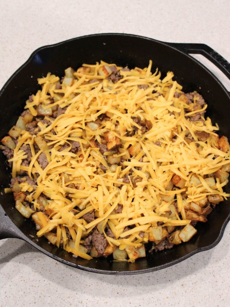 cheese added to the potato and meat mixture ready to boil in the cast iron pan. 