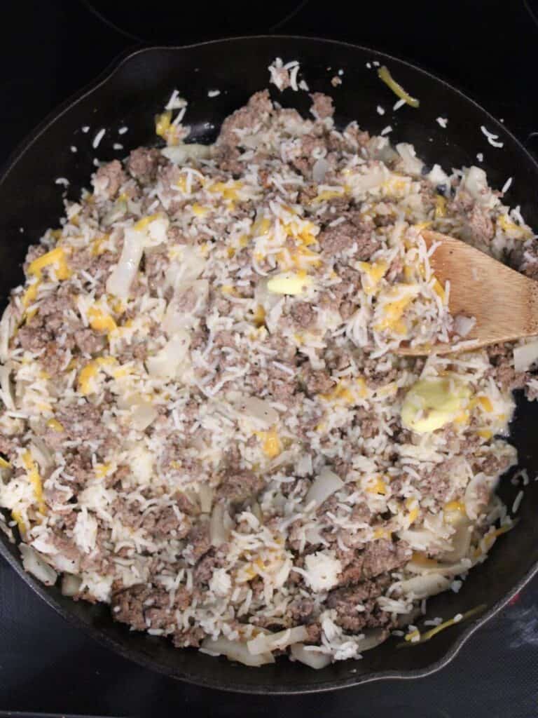 Adding milk and cheese to the ground beef mixture in a cast-iron pan with wooden spoon