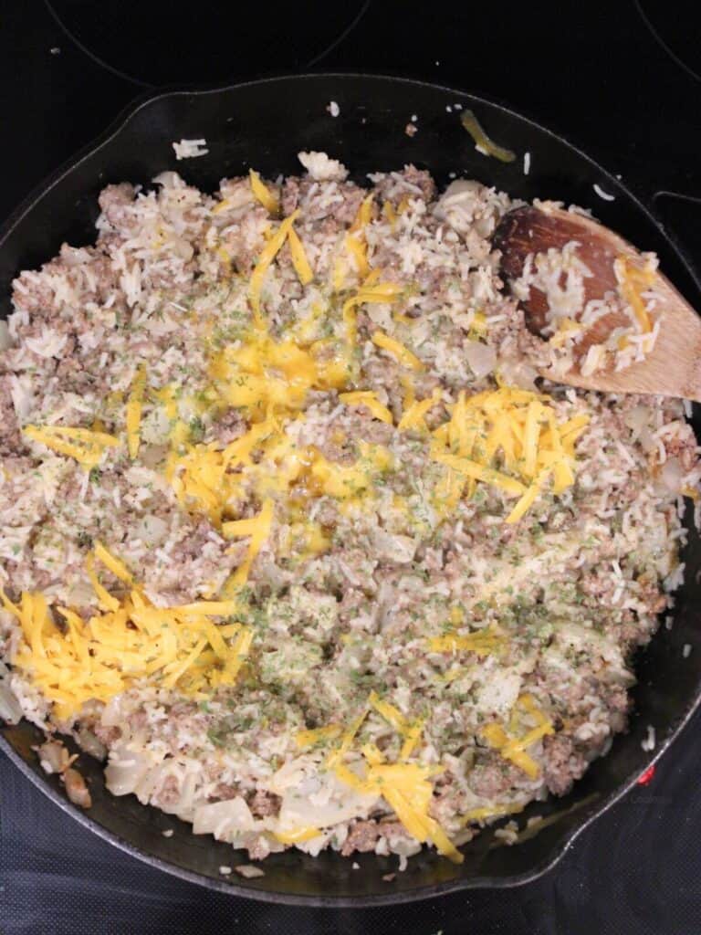 Topping the ground beef mixture with extra cheese in a cast-iron pan and wooden spoon