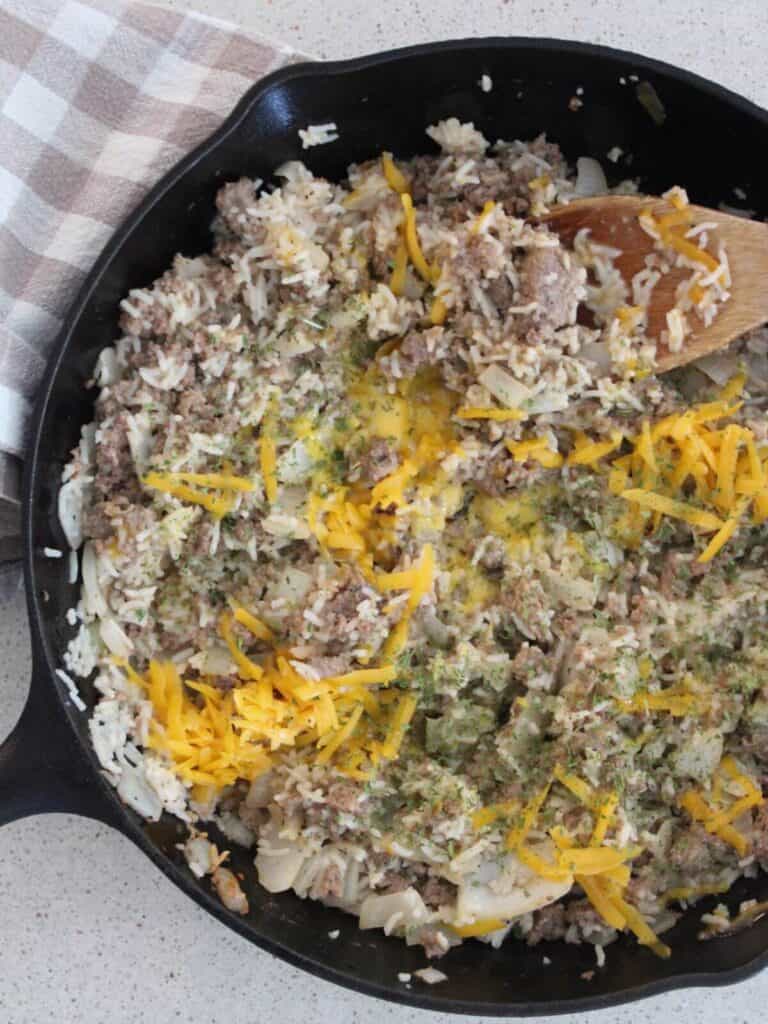 Cheesy Rice with Beef ready to eat in a cast-iron dish with a wooden spoon and plaid towel next to it.