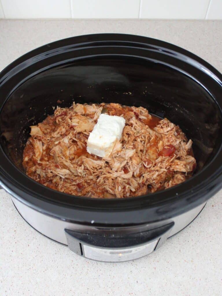 Adding cream cheese to the shredded chicken in the crockpot.