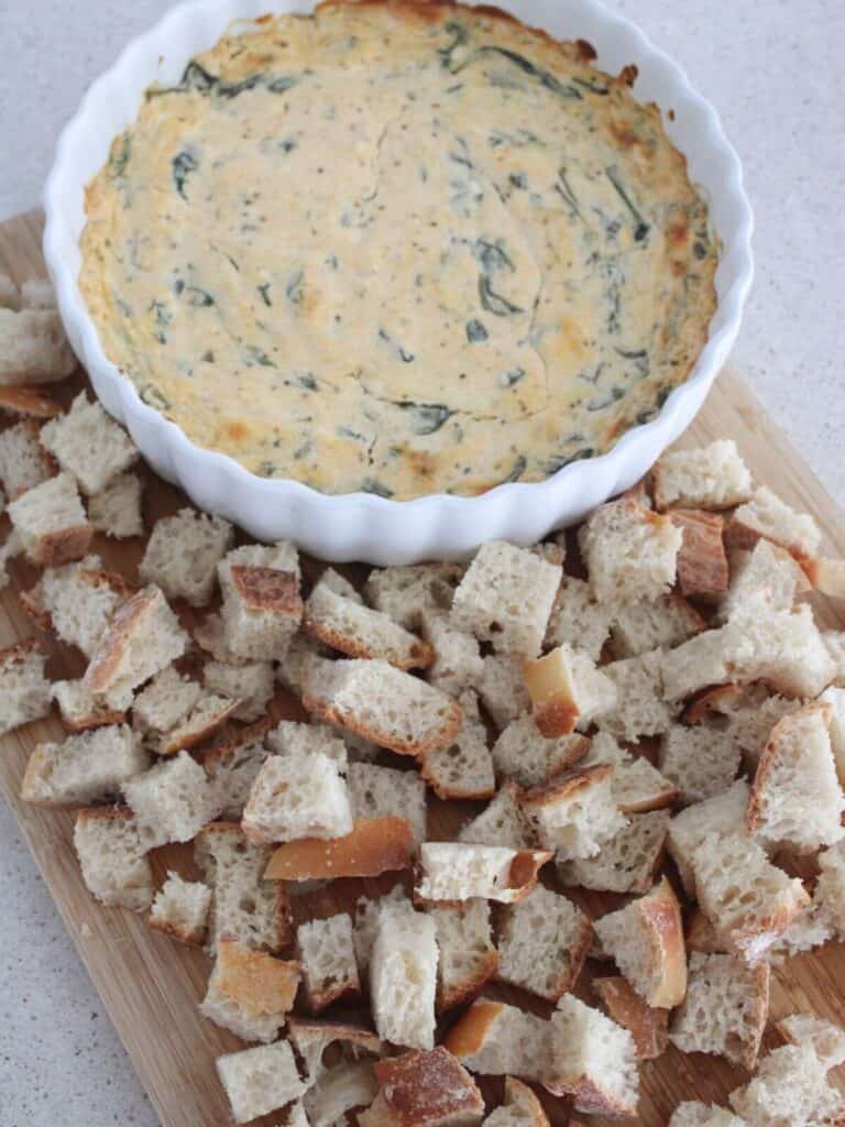 Spinach Dip in a white bowl on a cutting board with sourdough bread around it. Ready to serve. 