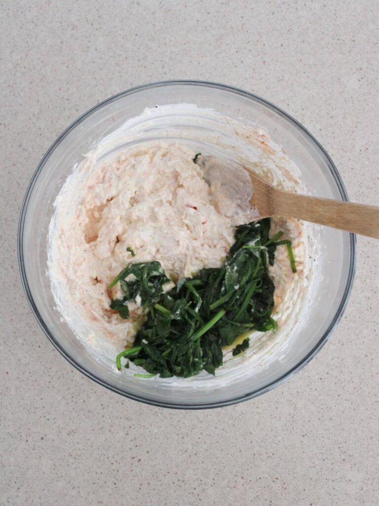 spinach being folded into the mixture in a glass bowl with a wooden spoon. 